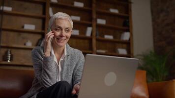 Smiling Senior Woman on Phone Call While Working on Laptop video