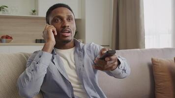 Young african american man having a conversation with a cable network support while using tv remote video