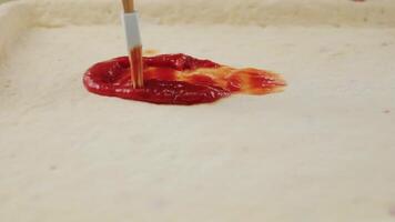 man applies ketchup to a thick piece of dough, smearing it with a grease brush. The cook smears the sauce. The concept of fast food video
