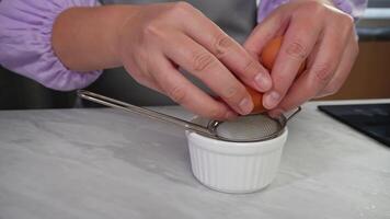 Hands cracking egg into strainer over bowl in kitchen setting , step 2. video
