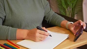 Woman taking notes with marker while using smartphone in cozy setting video