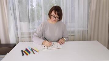 Woman coloring mandala at table with bright markers in relaxing home setting video