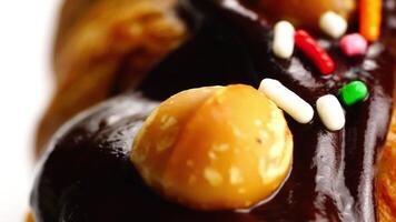 Extreme closeup view rotation of chocolate butter bun garnished with nuts and rainbow sprinkles pouring with chocolate syrup. video