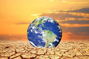 A symbolic image depicting a globe resting on cracked, arid earth against a fiery sunset. A poignant visual representing climate change photo