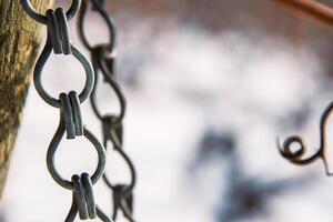 Closeup of vineyard trellis end posts chains hanging on a snowy branch in winter. Vineyard covered with snow on the blurred background. Metal construction component. Copy space photo