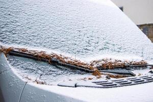 Snow covered frosty car windshield with leaves on wipers. Winter traffic in snowfall. Challenging driving conditions, icy roads, and seasonal weather impacts on transportation. Copy space photo