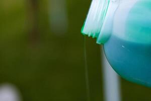 Closeup of vibrant green detergent pouring from a white plastic bottle against a blurred background. Green liquid flowing from a container. Copy space. Selective focus photo