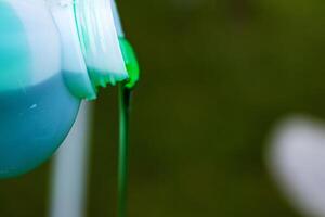 Closeup of vibrant green detergent pouring from a white plastic bottle against a blurred background. Green liquid flowing from a container. Copy space. Selective focus photo