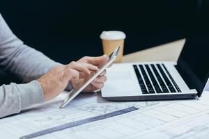 Close-up photo of hands of male designer architect working with tablet computer inside modern office.