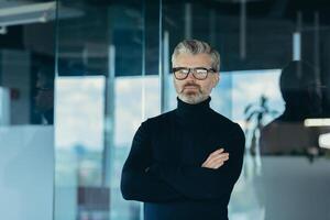 Portrait of serious and focused businessman with crossed arms, man working in office wearing glasses looking at camera, successful thoughtful investor photo