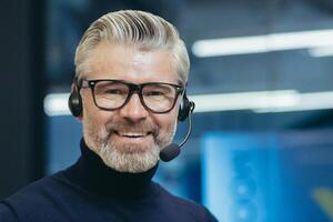 Closeup portrait of senior mature boss with headset, call, man smiling and looking at camera, gray haired businessman wearing glasses manager investor working inside modern office building, photo