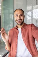 Confident individual engaging in a call, waving hello with a smile. Capturing connections and warmth in a clear and professional environment emphasizing communication. photo
