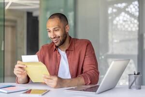 A cheerful man opening and reading an envelope at his office desk. He appears pleased with the contents, symbolizing success, important news, or professional correspondence in a lively workspace. photo