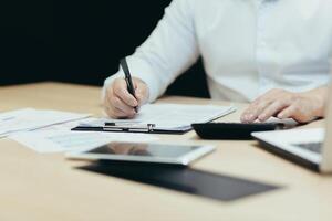 Close-up photo. Man's hands in a white shirt of an accountant, auditor, financier, banker working in the office at a table with documents and with a laptop, using a calculator. photo