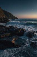 Serene coastal landscape at twilight with crashing waves and rocky cliffs. photo