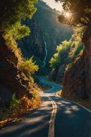 A winding road through a lush canyon with sunlight and a waterfall in the background. photo