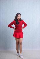full body expression of young Asian woman wearing red sweater, standing smiling with both hands holding waist to camera, isolated on white background photo