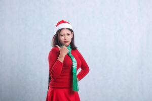 expression of young indonesia woman wearing christmas sweater, santa hat and scarf, slanting left pouting to camera hand sign pointing to right, isolated on white background photo