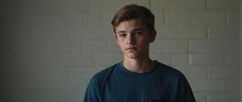 A young man is standing in front of a brick wall photo