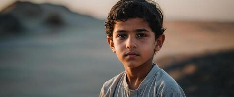 A young boy stares into the camera while standing in the desert photo