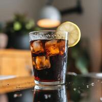 A glass of cola with ice and lemon on a table photo