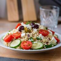 A plate of couscous salad with cucumbers, tomatoes and olives photo