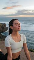A woman is sitting on a rock near the ocean photo