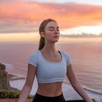 A woman in a white top is meditating in front of the ocean photo