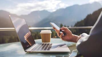 A man using his laptop and mobile phone in front of a mountain view photo