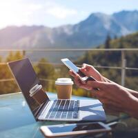 A man using his laptop and mobile phone in front of a mountain view photo