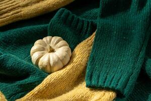 White pumpkin near a stack of knitted sweaters on a knitted blanket photo