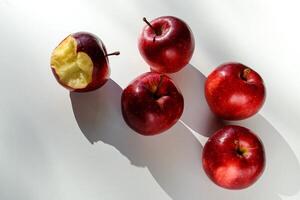 Five red ripe apples lying on a white table and their shadows photo