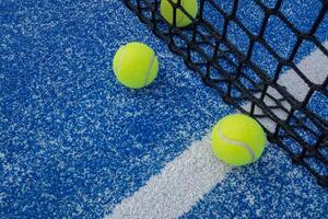 Three yellow balls on floor in front and behind of paddle net in blue court outdoors. Padel tennis court photo