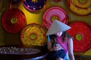 Traditional vietnamese hat. holds a phone in his hands, sits. Travel to asia Girl in Vietnamese hat with phone photo
