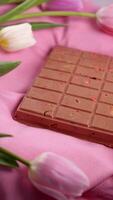 A bar of pink ruby chocolate with sublimated freeze-dried strawberries and almonds and spring tulip flowers . A dessert based on berries and nuts for International Women's Day, March 8, mother's day photo