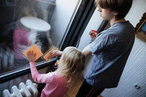 Children cleaning a large window together on a sunny afternoon in a cozy home photo
