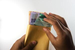 Hands Counting Colorful Banknotes Inserted in a Yellow Envelope on White Background photo