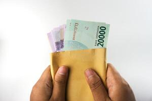Hands Holding Indonesian Rupiah Banknotes in an Envelope Against White Background photo