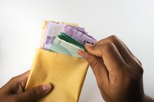 Hands Counting Colorful Banknotes Inserted in a Yellow Envelope on White Background photo