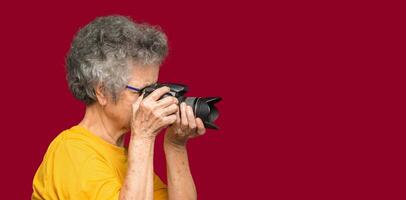 Senior woman taking photographs with a digital camera while standing on a red background photo