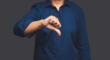 Negative concept. Close-up of businessman hand in a blue shirt showing thumbs down while standing on a gray background photo