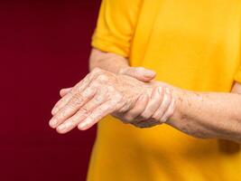 Senior woman suffering from wrist pain while standing against a red background photo