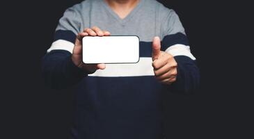 Hand holding a horizontal mobile phone with a blank white screen and showing thumbs up while standing on a black background photo