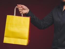 Hand holding a yellow and red paper bag with a handle while standing on a red background photo
