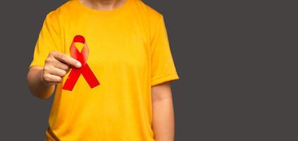 Hand holding a red ribbon for December World AIDS Day while standing on a gray background photo