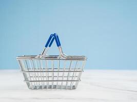 An empty mini shopping cart over a marble floor with a light blue background photo