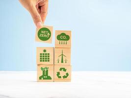 Net-zero CO2 emissions target in 2050. Hand holding of a wooden cube with green icons over a marble floor against a light green background photo