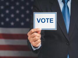 Close-up of hand voter holding paper with text VOTE while standing on the American flag background photo