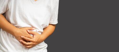 A man suffering from abdominal pain used hands to hold his belly while standing on a gray background photo