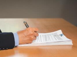 Close-up of a businessman signing on documents while sitting working in the office photo
